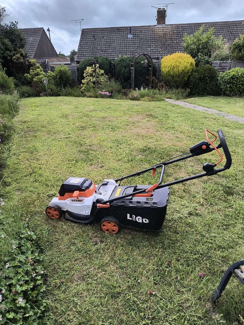 The same lawn freshly mown, neat archway and shrubs in the background, the mower parked on the cut grass.